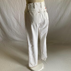 May include: White denim jeans with a high waist and classic five-pocket design. The jeans are displayed on a mannequin, showcasing the fit and style. The stitching and details are visible, highlighting the quality of the garment.