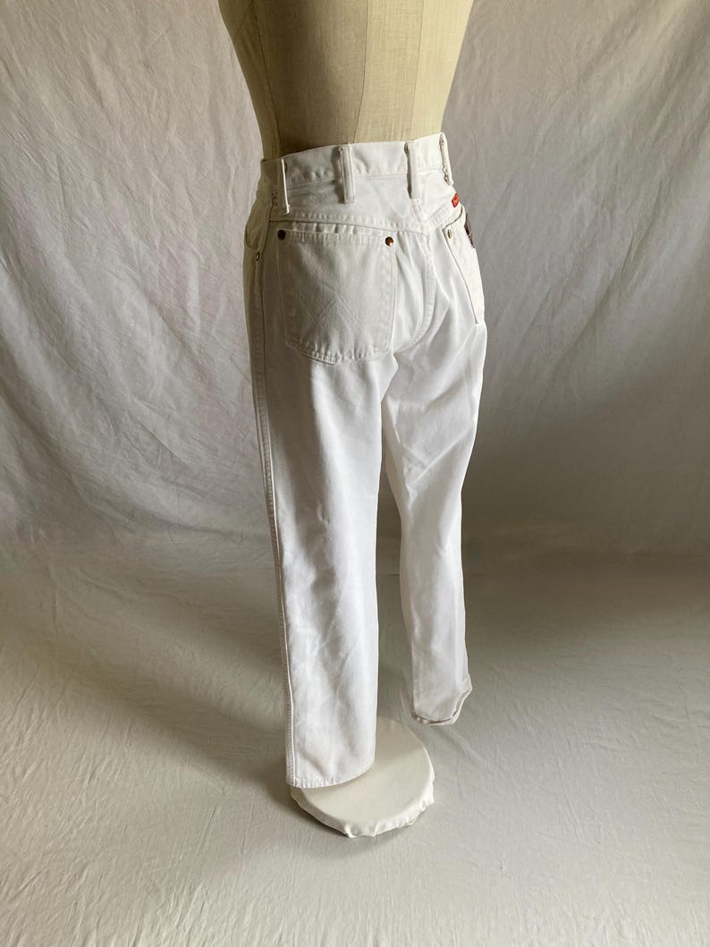 May include: White denim jeans with a high waist and classic five-pocket design. The jeans are displayed on a mannequin, showcasing the fit and style. The stitching and details are visible, highlighting the quality of the garment.