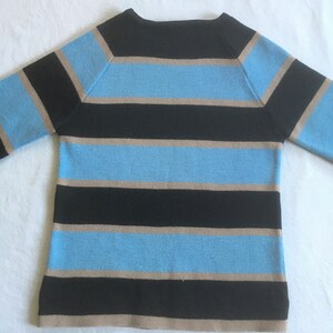 May include: A striped sweater with black, light blue, and beige horizontal stripes. The sweater has a boat neck and long sleeves.