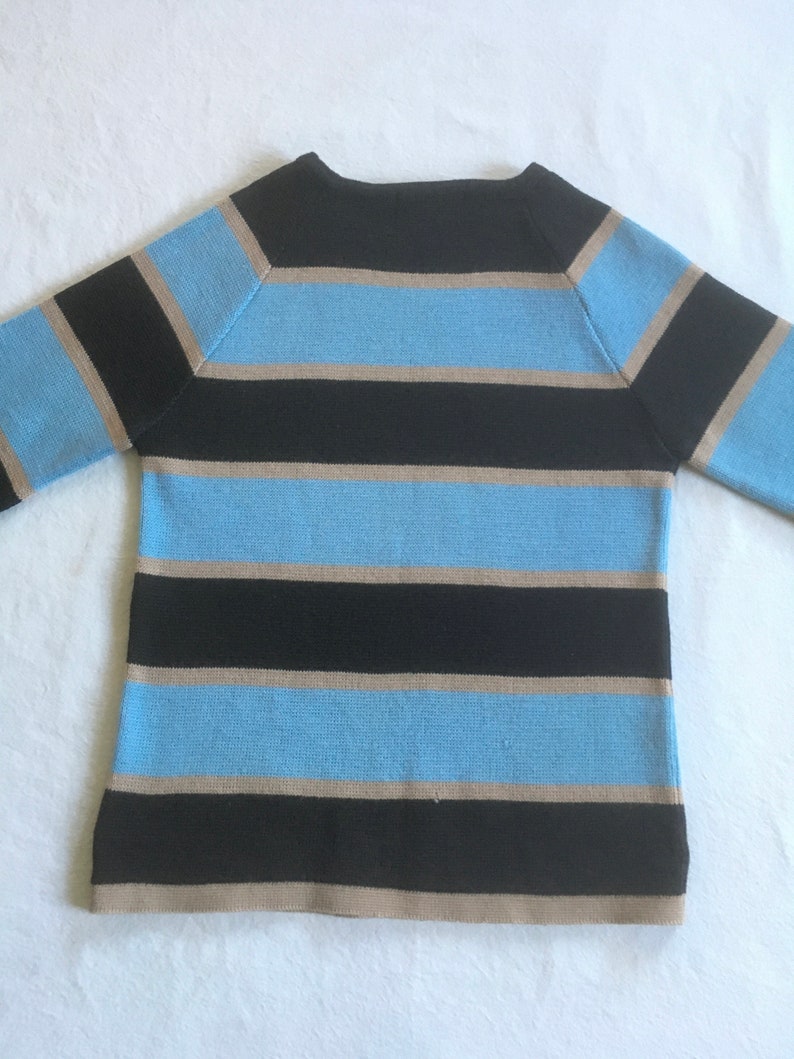 May include: A striped sweater with black, light blue, and beige horizontal stripes. The sweater has a boat neck and long sleeves.