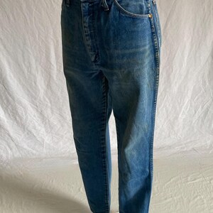 Pu&ograve; includere: Jeans blu in denim con un classico design a cinque tasche. I jeans hanno una chiusura con bottone e cerniera e una vestibilit&agrave; dritta. Il denim ha un aspetto sbiadito, con alcune aree pi&ugrave; chiare. I jeans sono esposti su un manichino.