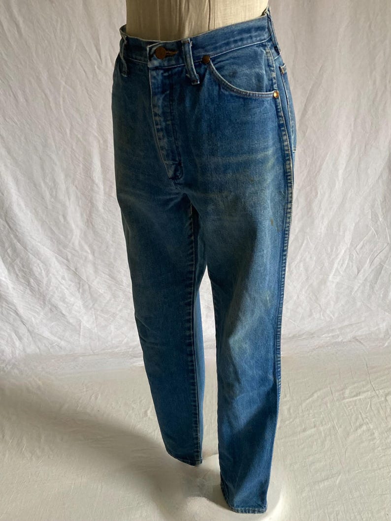 Pu&ograve; includere: Jeans blu in denim con un classico design a cinque tasche. I jeans hanno una chiusura con bottone e cerniera e una vestibilit&agrave; dritta. Il denim ha un aspetto sbiadito, con alcune aree pi&ugrave; chiare. I jeans sono esposti su un manichino.