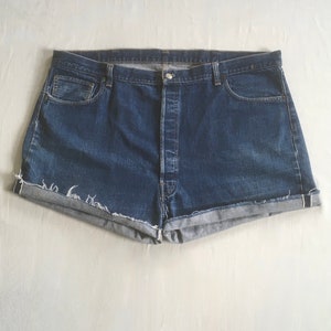 Puede incluir: Un par de pantalones cortos de mezclilla azul con cierre de botón y bordes deshilachados.