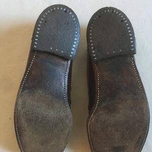 May include: A pair of brown leather shoes with white stitching around the edges of the soles. The soles are worn and have a pattern of small holes.