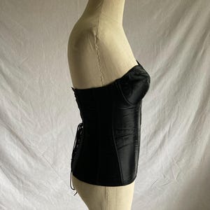 May include: A black satin corset with a lace-up back and a boned structure. The corset is displayed on a white mannequin.