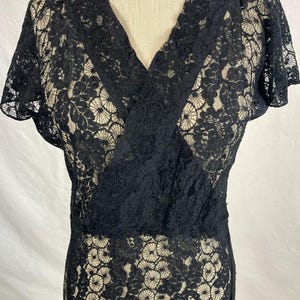 May include: A black lace dress with a V-neckline and short sleeves. The dress is made of a delicate, sheer lace fabric.