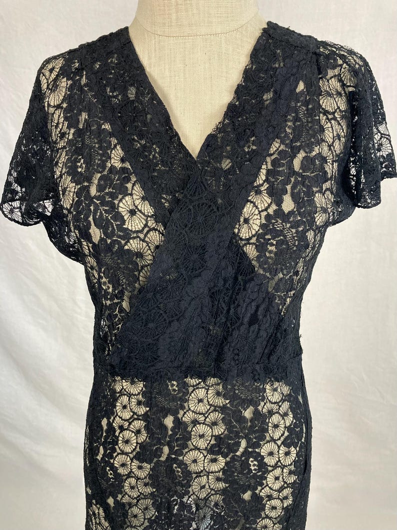 May include: A black lace dress with a V-neckline and short sleeves. The dress is made of a delicate, sheer lace fabric.