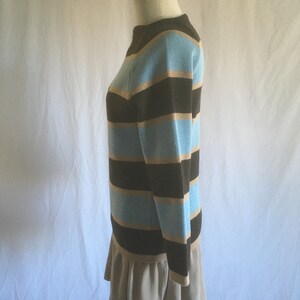 May include: A striped sweater with brown, light blue, and beige stripes. The sweater has long sleeves and a round neckline.