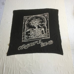 May include: Black fabric with a white graphic of a skeleton with a tree growing out of its head. The text "Grateful Dead" is printed below the graphic.