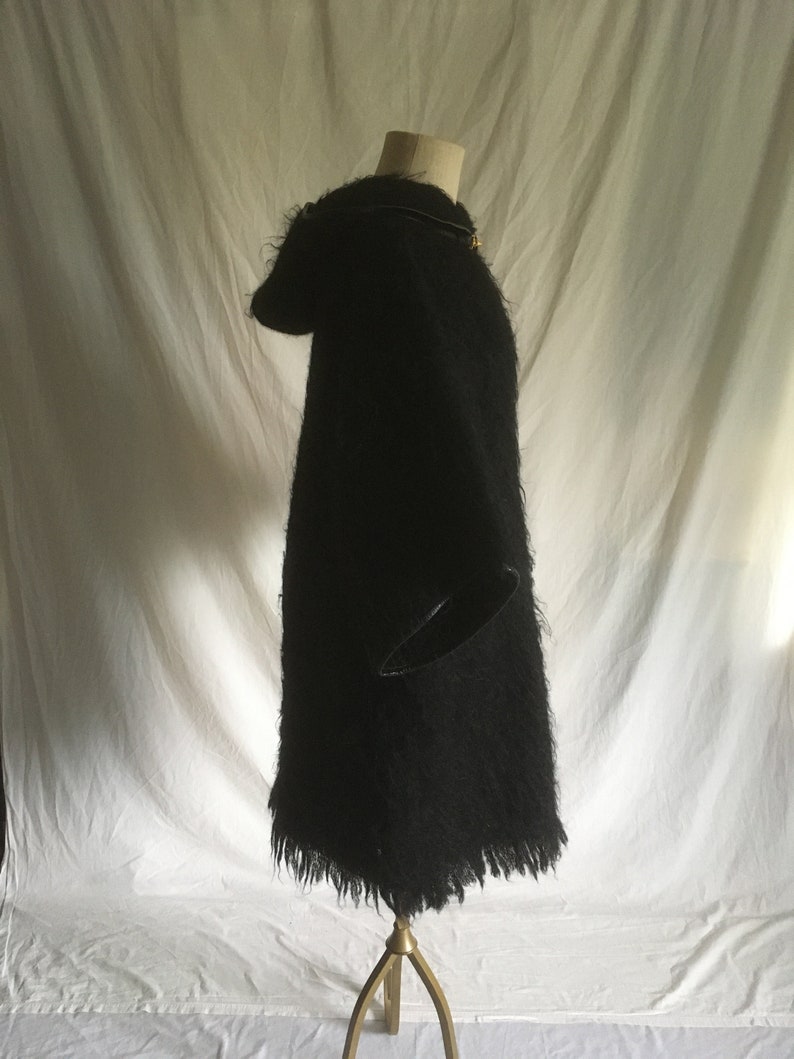 May include: A black fuzzy hooded sweater with a long fringe hem. The sweater is on a mannequin and is photographed against a white backdrop.