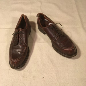 May include: A pair of brown leather lace-up shoes with a pointed toe. The shoes are worn and have some scuffs and scratches.