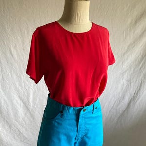 May include: A red short-sleeved top paired with bright blue pants. The top has a round neckline and a simple design. The pants have a classic five-pocket design. The outfit is displayed on a mannequin.
