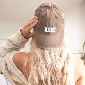 Puede incluir: Una gorra de b&eacute;isbol marr&oacute;n con la palabra "BABE" bordada en blanco en la parte delantera.