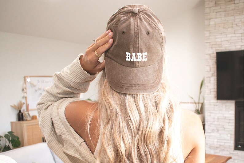 Puede incluir: Una gorra de b&eacute;isbol marr&oacute;n con la palabra "BABE" bordada en blanco en la parte delantera.