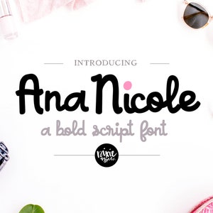 May include: Introducing Ana Nicole, a bold script font. The text is in black with a pink dot above the word "Nicole". The text is on a white background with various objects around it, including a pair of sunglasses, a piece of fabric, and a plant.