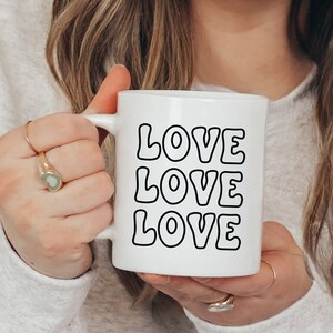 以下が含まれることがあります： レトロなフォントで「LOVE LOVE LOVE」と書かれた、黒いアウトラインの文字が入った白いセラミックマグカップです。