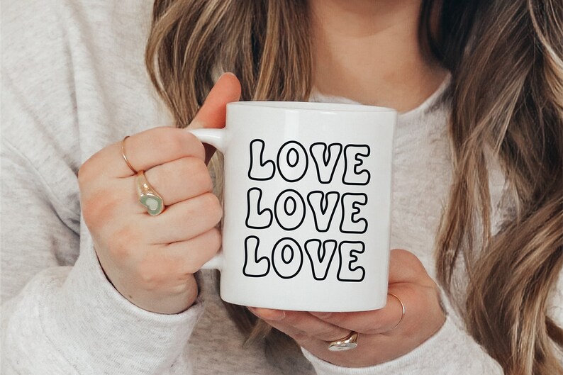 以下が含まれることがあります： レトロなフォントで「LOVE LOVE LOVE」と書かれた、黒いアウトラインの文字が入った白いセラミックマグカップです。