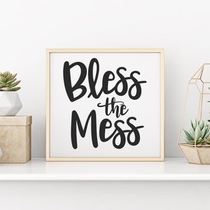 May include: A framed print with the text "Bless the Mess" in black script font on a white background. The print is displayed on a white shelf with two potted succulents and a gold geometric terrarium.