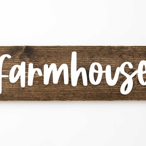 May include: A rustic wooden sign with the word "farmhouse" painted in white on a dark brown background.