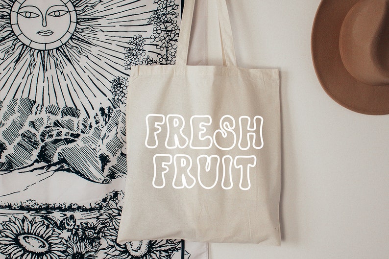 以下が含まれることがあります： 白いキャンバス地のトートバッグに、白い輪郭の文字で「FRESH FRUIT」と印刷されています。