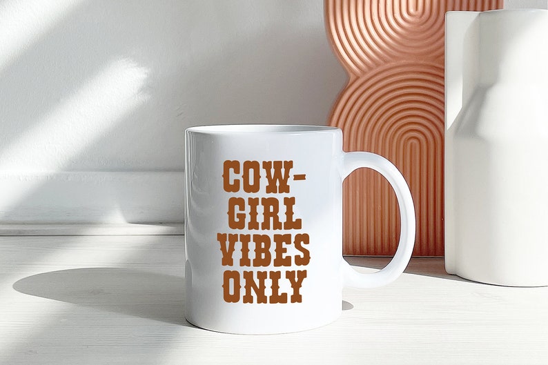 Puede incluir: Taza de cer&aacute;mica blanca con un gr&aacute;fico marr&oacute;n que dice "COW-GIRL VIBES ONLY".