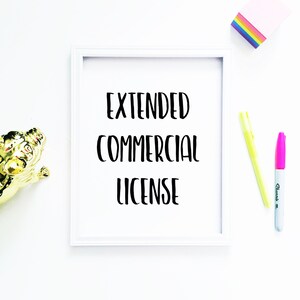 May include: White frame with the text "EXTENDED COMMERCIAL LICENSE" in black lettering on a white background. The frame is on a white surface with a gold figurine, a pink highlighter, and a yellow highlighter.