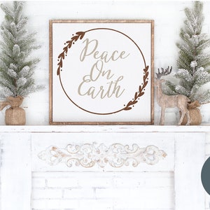 Pu&ograve; includere: Un cartello di legno bianco con un cerchio marrone e il testo "Peace On Earth" in un font beige. Il cartello &egrave; decorato con rami marroni con foglie. Il cartello &egrave; appoggiato su un camino bianco con un piccolo pino innevato su ogni lato.