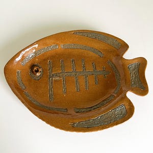 May include: A brown ceramic fish-shaped dish with a gray glaze. The dish has a raised fishbone design in the center.