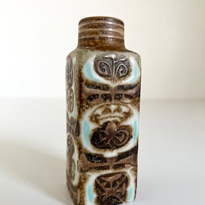 May include: A small, rectangular ceramic vase with a brown and white geometric pattern. The vase has a light blue glaze in the design.