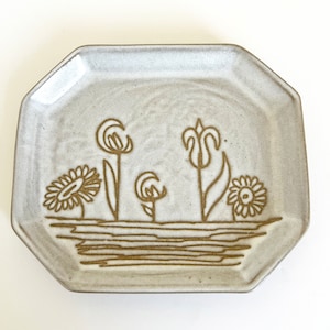 May include: A white ceramic octagonal plate with a brown floral design. The plate features stylized flowers and leaves.