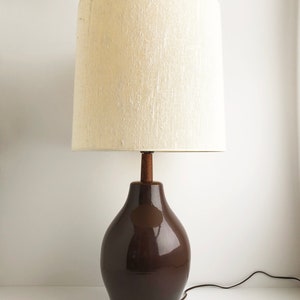May include: A brown ceramic table lamp with a white linen lampshade. The lamp has a rounded base and a wooden finial.