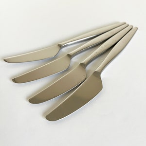May include: Four silver butter knives with slightly rounded edges and a polished finish.