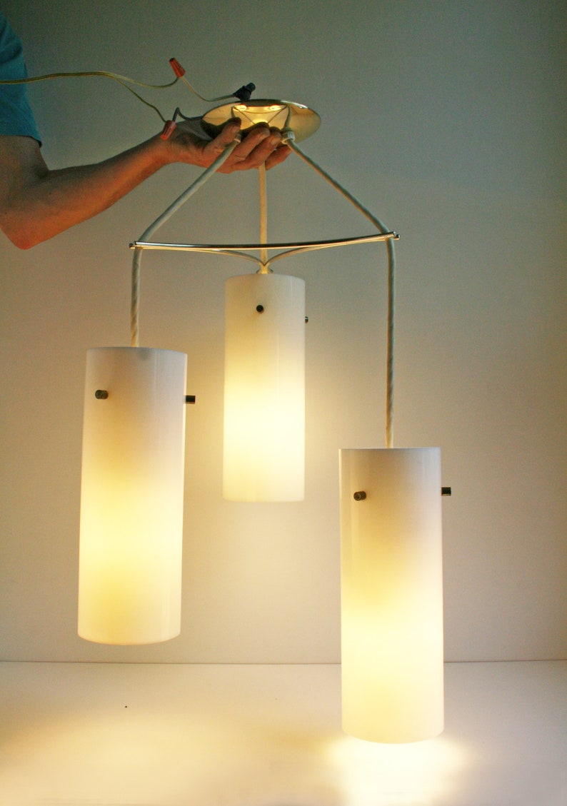 May include: A three-light pendant light fixture with white frosted glass shades. The shades are cylindrical and hang from a metal frame.