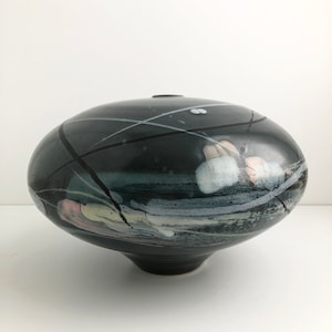 May include: A black ceramic vase with a wide, rounded base and a narrow opening. The vase is decorated with white and pink abstract lines and shapes.