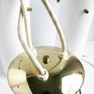 May include: A gold-colored ceiling light fixture with three white glass shades and white cords. The fixture has a round, flat base.