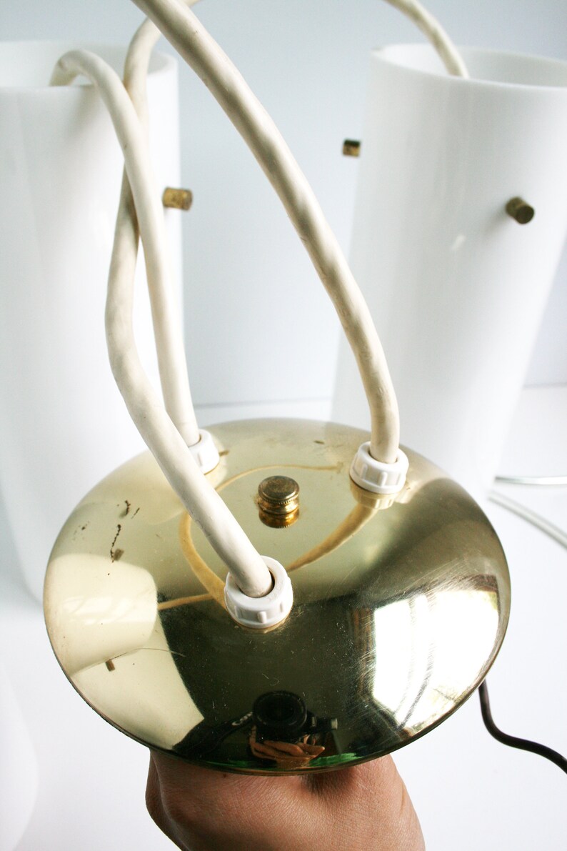 May include: A gold-colored ceiling light fixture with three white glass shades and white cords. The fixture has a round, flat base.