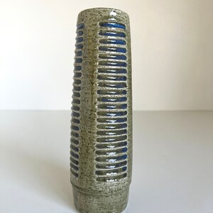 May include: A tall, cylindrical ceramic vase with a textured, green glaze and blue stripes. The vase has a slightly flared opening and a rounded base.