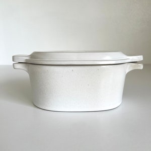May include: White oval ceramic baking dish with a lid. The dish has two handles on the sides and the lid has two handles on the top.