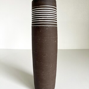 May include: A brown ceramic vase with white horizontal stripes. The vase has a textured surface.