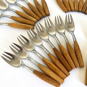 May include: A set of silver-toned forks and spoons with wooden handles. The forks and spoons are arranged in a fan shape on a white background.