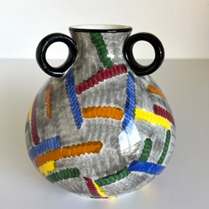 May include: A gray ceramic vase with two black handles. The vase is decorated with colorful stripes in red, yellow, blue, and green.