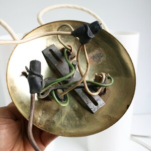 May include: Close-up of the underside of a brass ceiling light fixture with exposed wiring. The fixture has a circular base and a metal mounting plate. The wires are connected to the plate with black wire nuts.