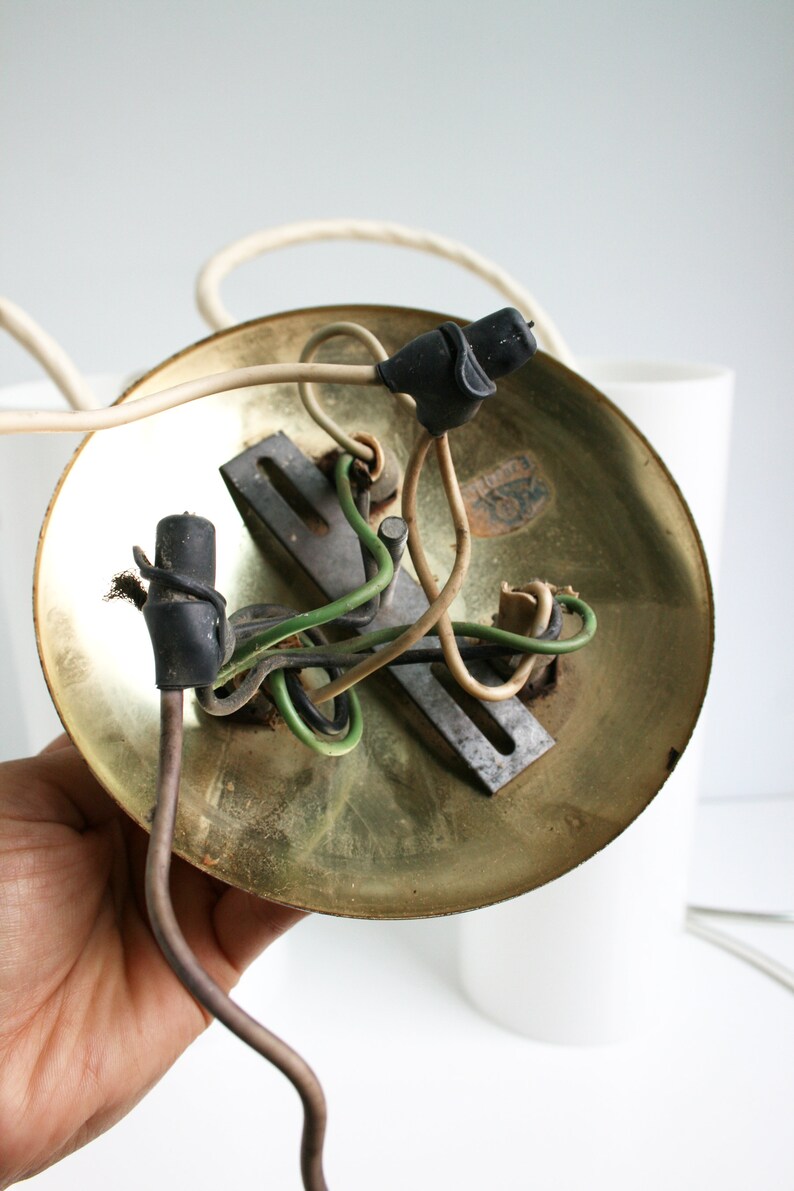 May include: Close-up of the underside of a brass ceiling light fixture with exposed wiring. The fixture has a circular base and a metal mounting plate. The wires are connected to the plate with black wire nuts.