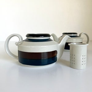 May include: Two white ceramic teapots with brown and blue striped designs and a matching white ceramic tea strainer.