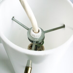 May include: Close-up of a white ceramic lampshade with a metal socket and wiring attached. The socket has three screws and a white plastic cover.