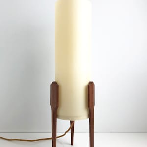 May include: A mid-century modern table lamp with a white cylindrical shade and a wooden tripod base.