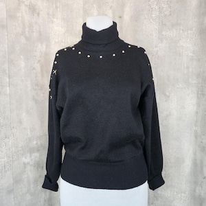 Könnte beinhalten: Schwarzer Rollkragenpullover mit goldenen Stern-Akzenten. Der Pullover hat eine gerippte Strickstruktur und eine figurbetonte Silhouette.