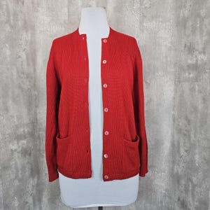 May include: A red knitted cardigan with a button-up front and two pockets. The cardigan is on a white mannequin.