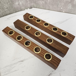 May include: Three wooden candle holders with a dark brown finish. Each holder has five brass-colored metal rings to hold candles. The holders are rectangular and have a beveled edge on one side.