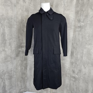 May include: A long, black coat with a buttoned collar and two front pockets. The coat is displayed on a mannequin against a gray background. The coat has long sleeves and a button closure.